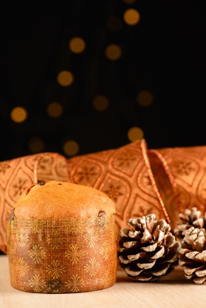 Small panettone next to pine cones and decorative ribbon and small lights