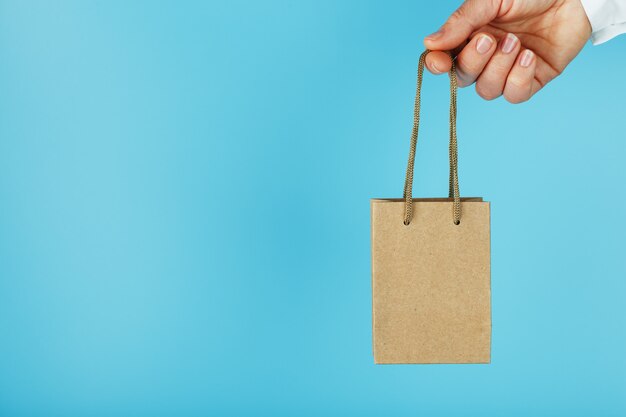 Small paper Bag at arm's length, brown craft bag for takeaway isolated on blue background. Packaging template layout with space for copying, advertising.