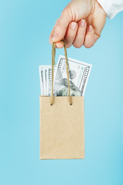 Photo a small paper bag for financial aid and support made of paper at arm's length with us dollars on a blue background. the concept of negligible financial support in business,