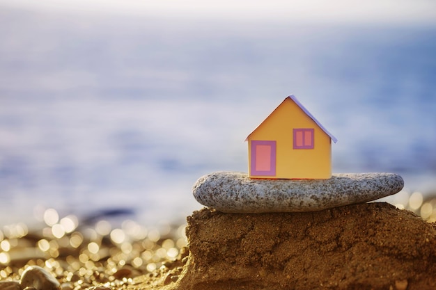 A small paper house against the backdrop of the sea at sunset the concept of real estate services a dream of a house by the se