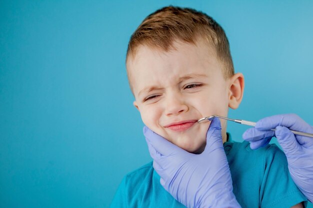 Photo small patient does not want to open the dentist's mouth on blue background dantist treats teeth close up view of dentist treating teeth of little boy in dentist office