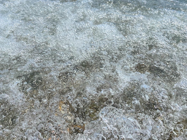 小さな小石と砂の海底の背景テクスチャを明確な浅い海の水のトップ ビューの下で