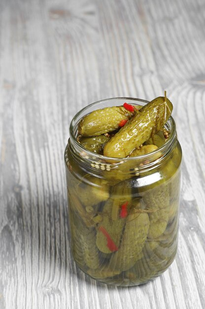 Small pickled cucumbers in glass jar on a wooden table