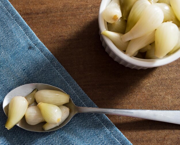 Small pickled onions in a spoon over a blue cloth and bowl with more onions