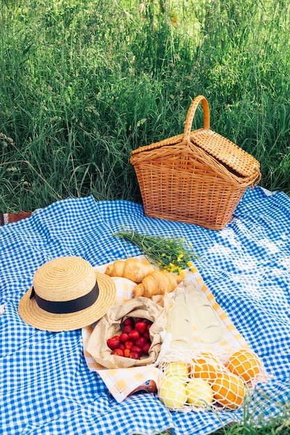 A small picnic with croissants strawberries and lemonade on a blue checkered blanket