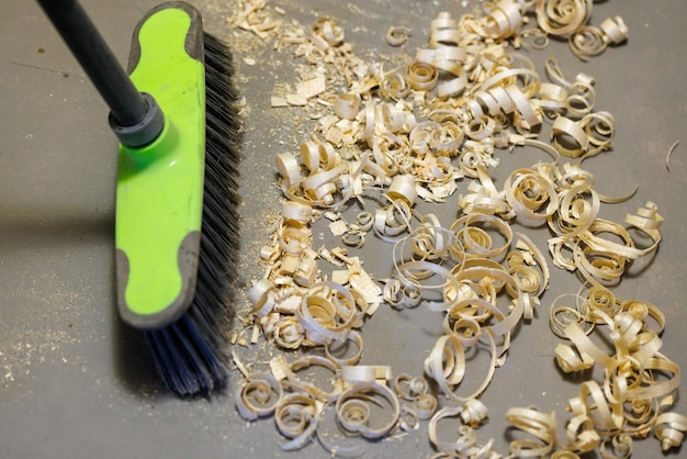 A small pile of wood shavings on a gray linoleum floor with a broom brush