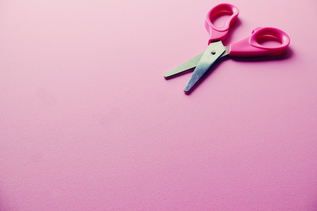 Small pink scissors on pink background close up