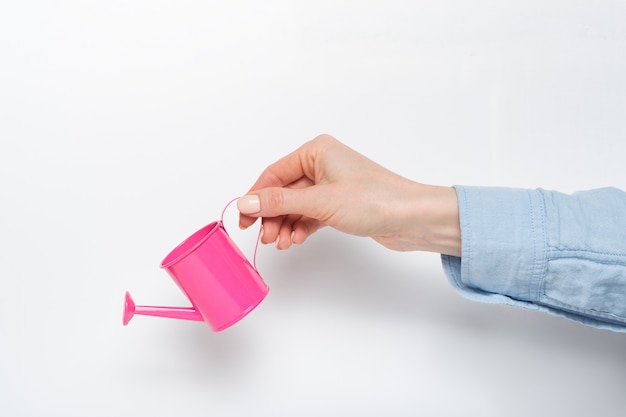 Small pink watering can in a female hand on a light