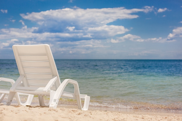 Small plastic deck chair standing on the sand of a beach against the sea.