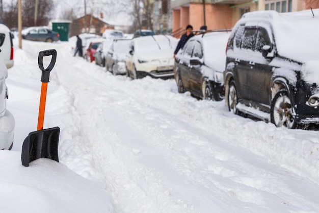 晴れた冬の朝に雪に覆われた車の近くに小さなプラスチック製のスノーショベル