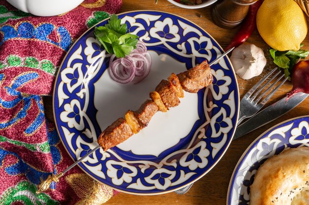 Foto una piccola porzione di shish kebab di agnello su uno spiedino con cipolla rossa e prezzemolo in una piastra con un modello nazionale uzbeko