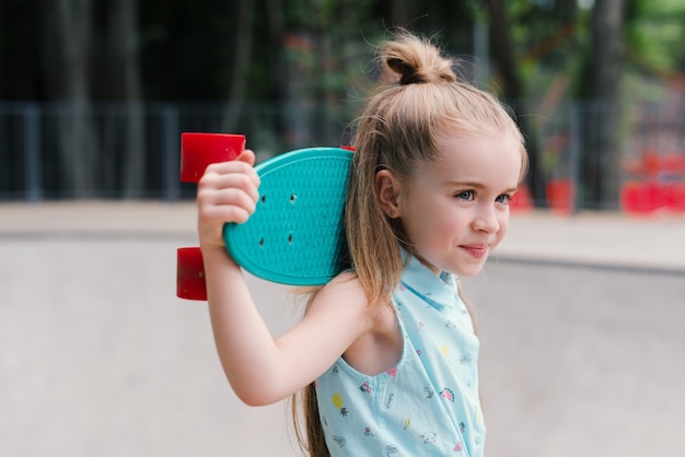 Photo small pretty girl holding a skateboard or penny board on a skate park