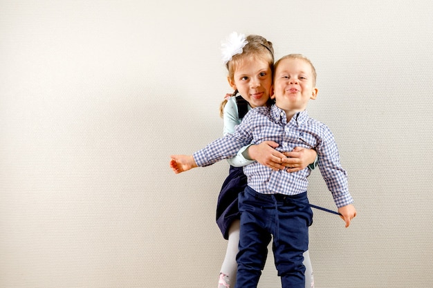 Small pretty girl standing near brother and hugging him while both are smiling and happy