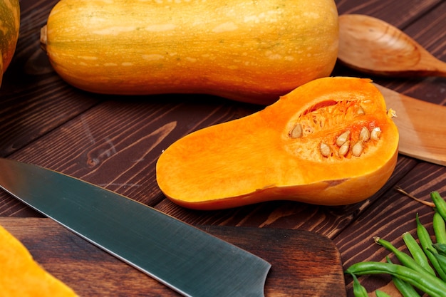 Small pumpkin cut into halves on wooden cutting board with knife