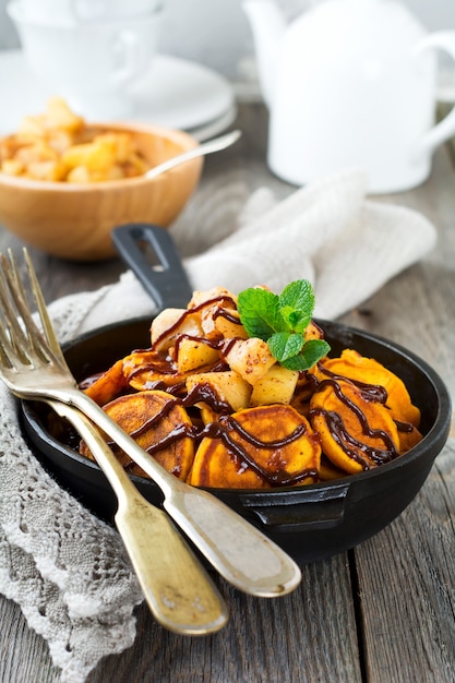 Small pumpkin pancakes with chocolate sauce in a pan on the old vintage wooden background.