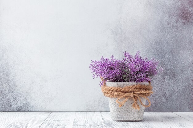 Piccoli fiori viola in vasi di ceramica grigi su sfondo di pietra stile rustico