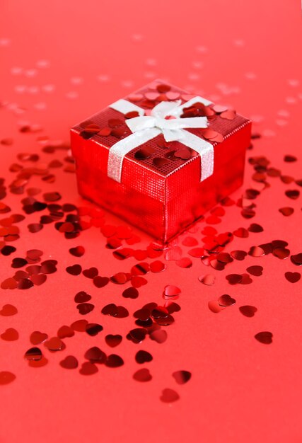 Small red gift box with silver ribbon on bright background with decorative small heart tinsel.