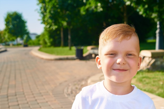 A small red-haired five-year-old boy stands in the park close-up