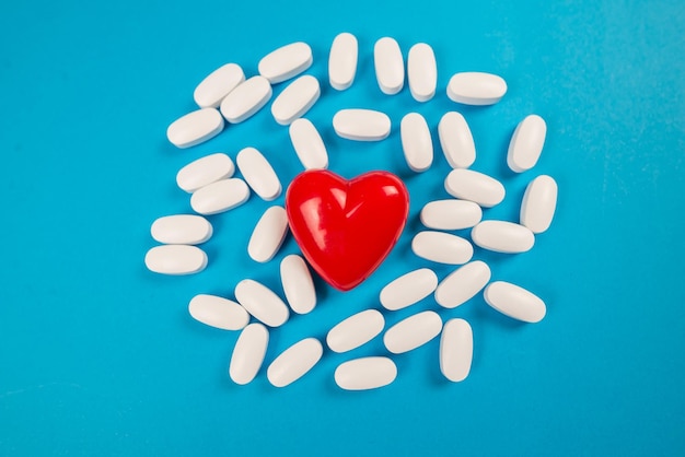 Small red heart and white pills on a blue background Medical concept