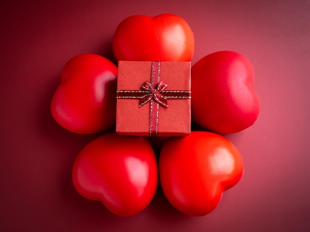 A small red present gift box with ribbon on five heart balls on\
red background an essential gift on special days with love\
birthdays new years valentine\'s day and anniversaries