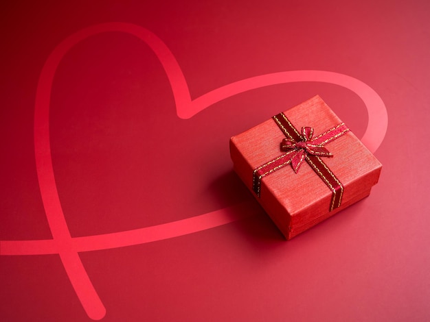 A small red present gift box with ribbon on heart shape drawing\
red background with copy space top view an essential gift on\
special days birthdays new years valentine\'s day and\
anniversaries