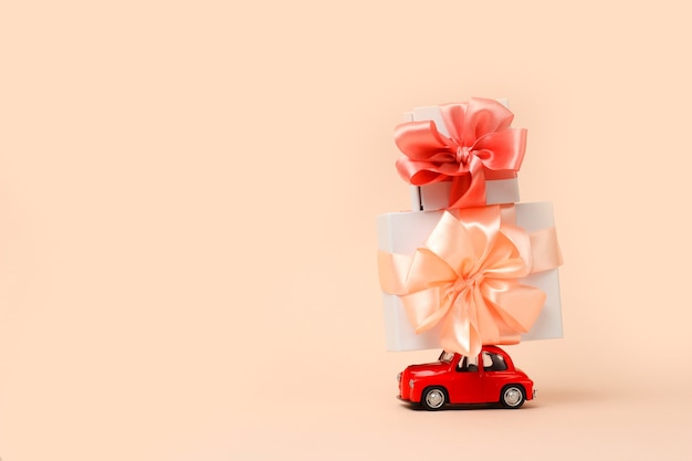 Small red retro toy car with a big gift on the roof on colal Delivery of gifts for Valentines Day  Christmas  World Womens Day  concept