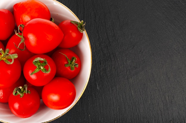 Piccoli pomodori ciliegia maturi rossi in una ciotola di insalata bianca.