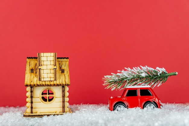 Фото Маленькая красная игрушечная машинка с елью на снежной дороге к деревянному дому