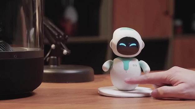 a small robot sitting on a round white table next to a monitor