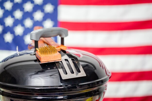 Small round charcoal grill and July 4th decorations on American flag background.