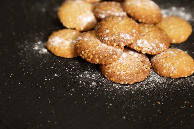 Маленькие круглые печенья с кунжутом посыпать сахарной пудрой на темном фоне.