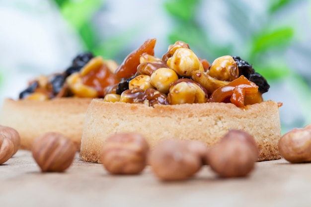 Маленькая круглая тарталетка с разнообразными начинками, хрустящая тарталетка с лесными орехами, арахисом и другими ингредиентами, тарталетка из теста с орехами и сухофруктами, покрытая карамелью
