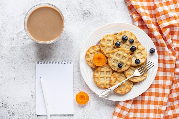 Small round waffles and a coffee on grey background, notebook, flat lay, copy space