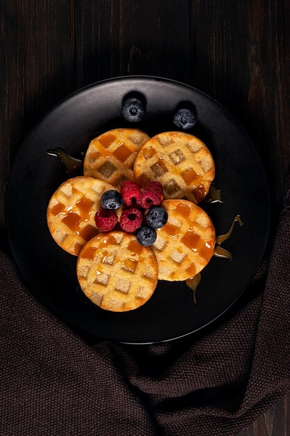 Small round waffles served with blueberries, raspberries and caramel sauce or honey. Copy space.