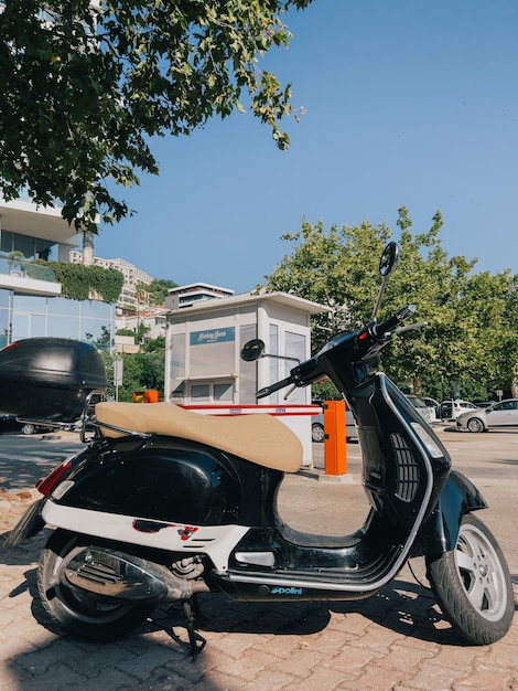 トランク付きの小型スクーターが木の近くの柵の駐車場に立っています。