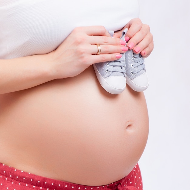 Small shoes for the unborn baby in the belly of pregnant woman