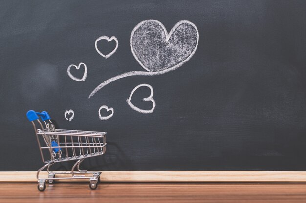 A small shopping cart and a heart shaped on a blackboard