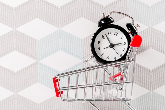 Small shopping cart with alarm clock. Shopping time concept