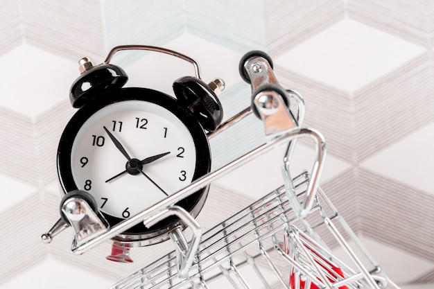 Photo small shopping cart with alarm clock. shopping time