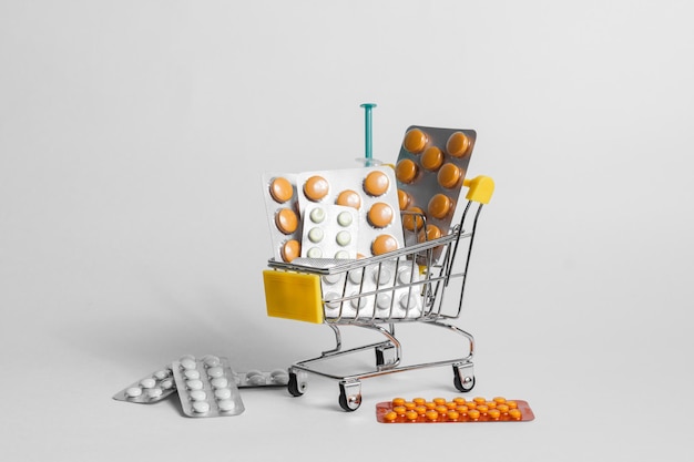 Small shopping cart with different medicines and syringe against white background in studio