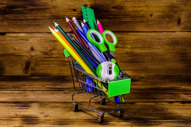 Small shopping cart with different school stationery on rustic wooden background. Back to school concept