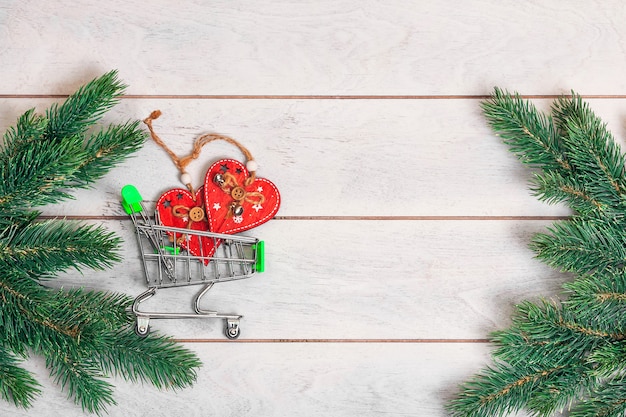 small shopping cart with gifts and fir branches on wooden background