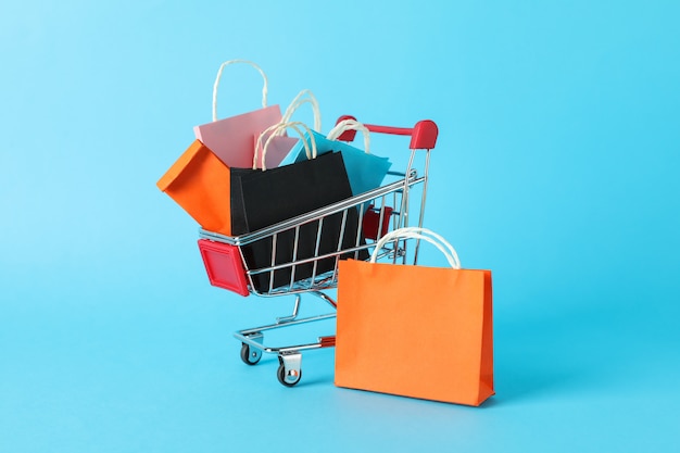 Small shopping cart with paper bags on blue space, space for text