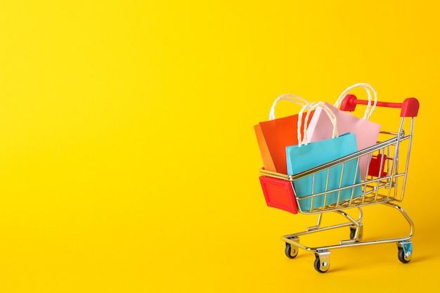 Small shopping cart with paper bags on yellow space, space for text