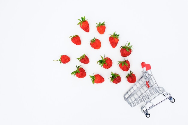 Small shopping trolley cart and flying scattering strawberries berry on white