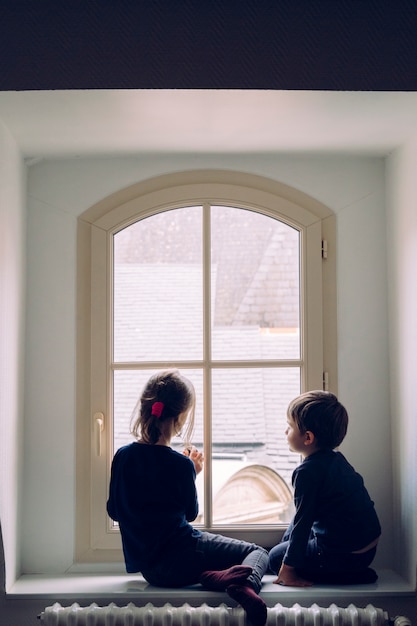 Small siblings looking through the window