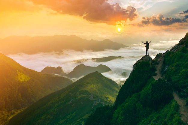 Small silhouette of tourist on rocky mountain with raised hands