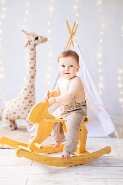 A small smiling baby boy is playing in the nursery a bright cozy children's room a child is riding a wooden rocking horse