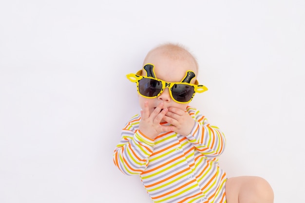 Small smiling baby girl lying on a white isolated background in bright sunglasses