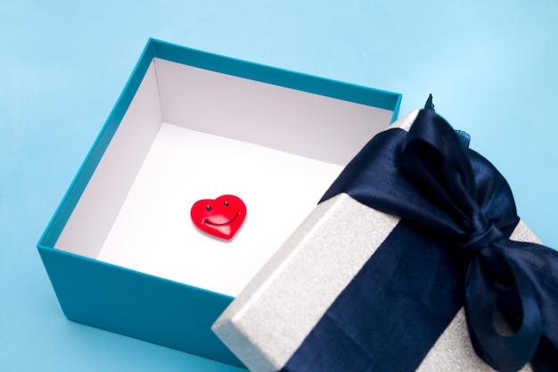 Маленькое улыбающееся сердце в подарочной коробке, синий фон, крупный план